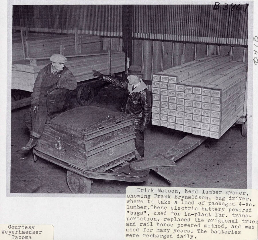 A photograph of head lumber grader Erick Matson with Frank Brynaldson who is the driver of the lumber bug. The lumber bug was powered by batteries that were recharged daily and moved lumber within the plant.