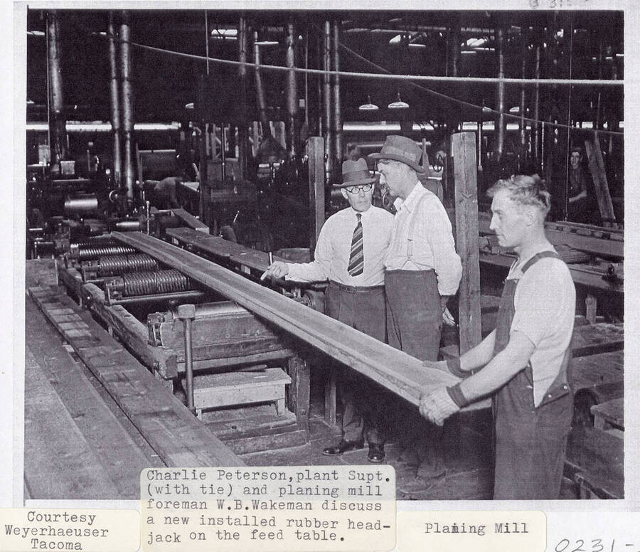 A photograph of plant superintendent Charlie Peterson and planing mill foreman W.B. Wakeman discussing a newly installed rubber head jack on the feed table.