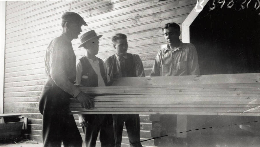 A photograph of planer foreman Bill Wakeman, replant foreman Guy Van Buskirk, inspector Howard Stafford, and dry sheds foreman Gus Hessel looking over a small load of lumber with a check grader.
