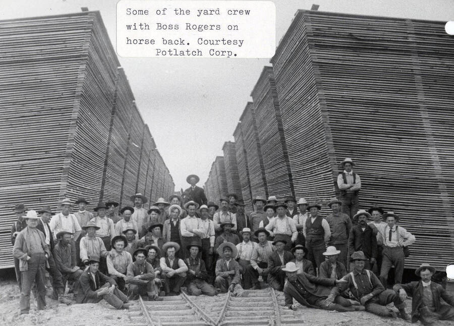 A photograph of the yard crew in the lumber yard with their boss Rogers on horse back.