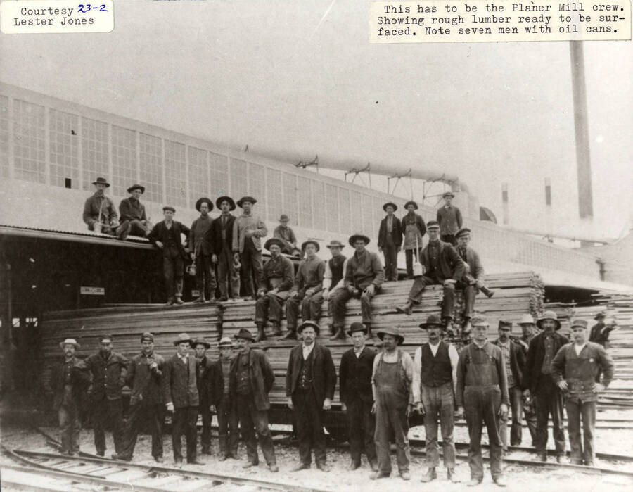 A photograph of the Planer Mill crew with rouch lumber ready to be surfaced. Seven men have oil cans.