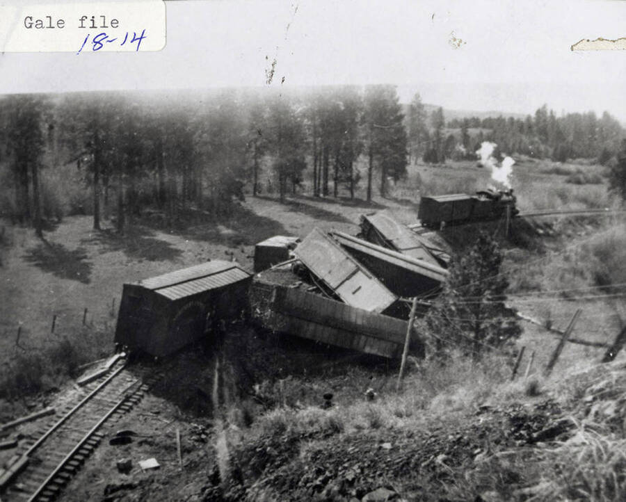 View of a train wreck. The locomotive can still be seen on the track, while the railroad cars can be seen piled up next to the track.