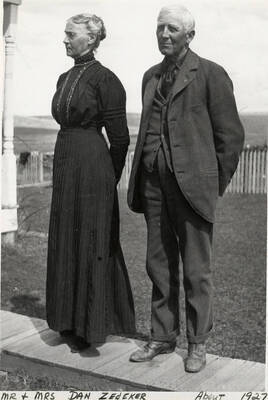 Mr. and Mrs. Dan Zedeker standing together for a photograph in front of their house and fields. Photograph taken around 1927.