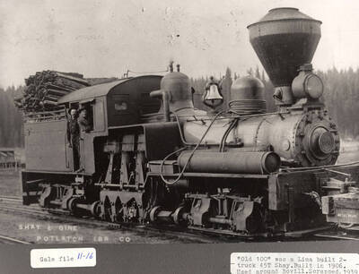 View of the 'Old 100', which was a Lima built 2-truck 45T Shay. It was built in 1906 to be used around Bovill for logging. A few logs can be seen in the back of the engine and two men can be seen leaning out the window of the engine.