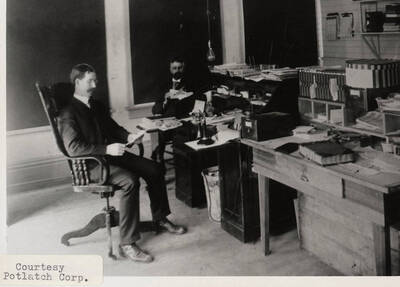 A photograph of two unknown men sitting and reading in an office.