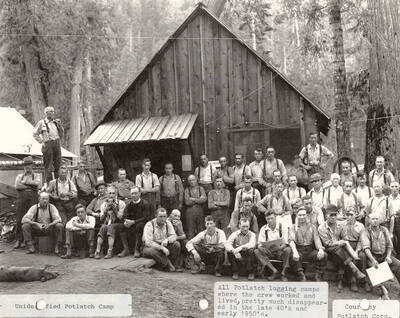 Group photo of the crew that worked and lived at the Potlatch camp. The men can be seen sitting and standing in front of a building.
