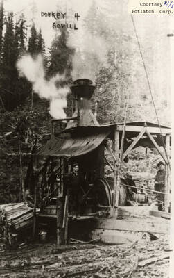 View of a few men standing around the steam donkey used in a camp located near Bovill, Idaho.