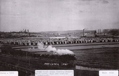 View of a WI&M mixed train leaving Potlatch going west bound. The mill and the town can be seen in the background.
