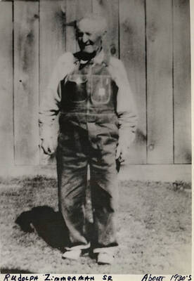 Rudolph Zimmerman Sr. standing in front of a wooden wall. Photograph taken around 1930.