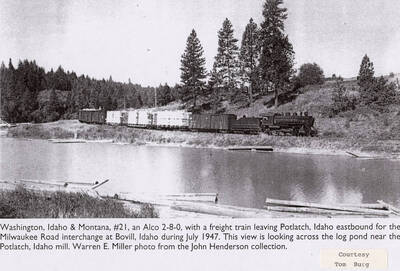 A WI&M No. 21 locomotive leaving Potlatch, Idaho heading eastbound for the Milwaukee Road interchange at Bovill, Idaho. The view looks across the log pond, which is located near the Potlatch mill.