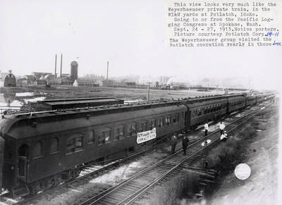 The Weyerhaeuser private train in the WI&M yards at Potlatch, Idaho. The train is going either to or from the pacific Logging Congress at Spokane, Washington. The Weyerhaeuser group visits the Potlatch operation yearly in late September. A few men can be seen standing and sitting on the railroad tracks next to the train.