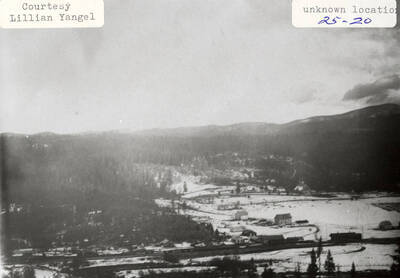 View of a town during the winter. The town is surrounded by hills and forests.