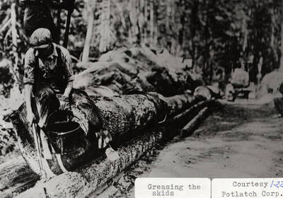 A man greasing the skids while sitting on top of a stack of logs.