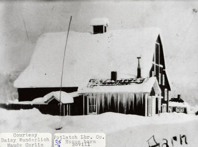 View of the Potlatch Lumber Company horse barn in Bovill, Idaho. The barn is covered in and surrounded by snow and icicles can be seen hanging off of the roof.