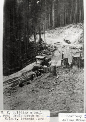M. K. building a railroad grade south of Helmer, towards Park. A man can be seen standing on a truck as it drives down the road.