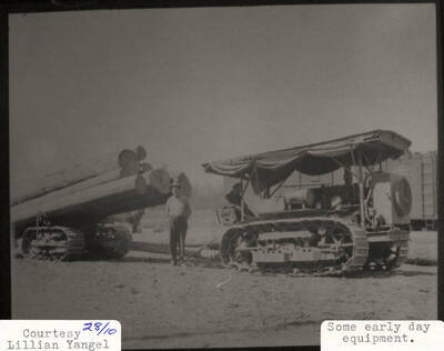 View of equipment used in the early days for logging. Men can be seen sitting and standing next to the equipment and a stack of logs can be seen sitting on top of it.