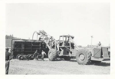 Two men pulling something away from the tipped rail car while others analyze the event.