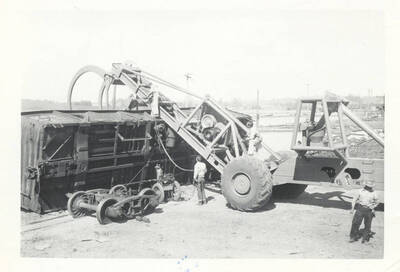 Workers inspecting the tipped rail car and the LeTourneau log unloading machine.