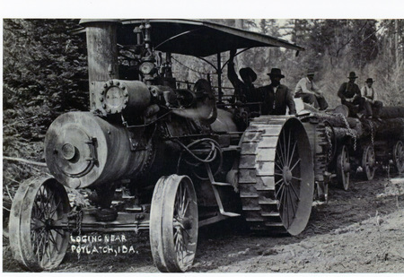 Photograph of a tractor with men pulling cars loaded with logs near Potlatch.
