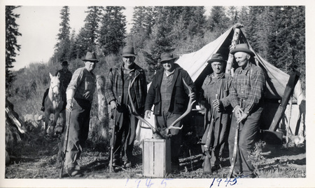 Photograph of a group of men at a hunting camp with antlers.