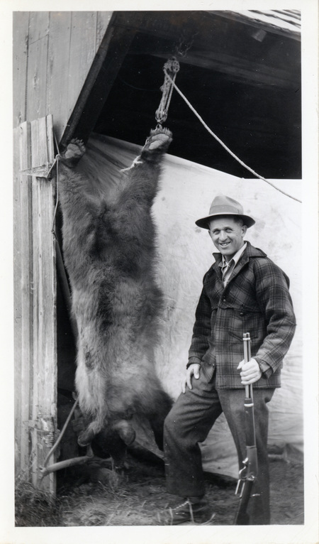 Photograph of Edward Bysegger displaying a bear skin at his hunting camp.