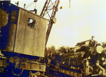 Photograph from slide of a loader and rail car with a man standing on logs.