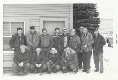 A group of thirteen men in coats to combat the cold weather.