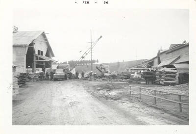 A road in a lumber yard leading to a truck with a crane like machine attached.