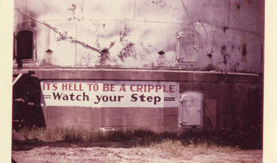 A photograph of a sign that reads, 'It's hell to be a cripple, watch your step.'
