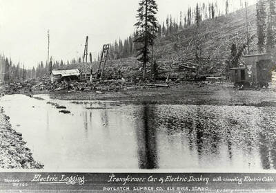 A photograph of a transformer car and electric donkey with a connecting electric cable at the Potlatch Lumber Company Elk River, Idaho Camp.Used for electric logging with E.J. Barry as the electrical engineer.