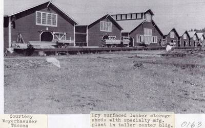A photograph of dry surfaced lumber storage sheds with a specialty manufacturing plant in the tall center building.