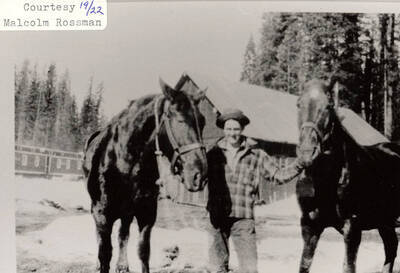 A man standing with two horses outside a log cabin at a PLC camp.