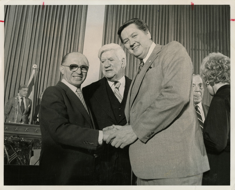 Photo Description: Two men shaking hands with a third person in between them. They're all posing for the photo. Text back translation "Menzchem begin, Prime minister of lsrael 1977 - 1983; Speaker of the House Tip O'neill (D) Speaker 1977-1987; Idaho Congressman George V. Hansen" Notes read on back "3x5 Greets Begin 88 1/2"