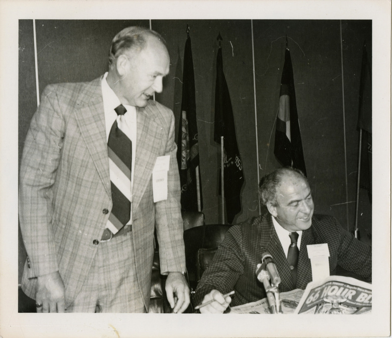 Photo Description: Idaho Governor Andrus and Nevada Governor O'Callaghan looking at a paper together and smiling. Text back translation "Governor Cecil D Andrus Nevada Governor Mike O'Callaghan" Notes read on back "15 3 2 Col x 4 [Illegible] Host Governor; 100 Nevada Gov - Mike O'Callaghan"