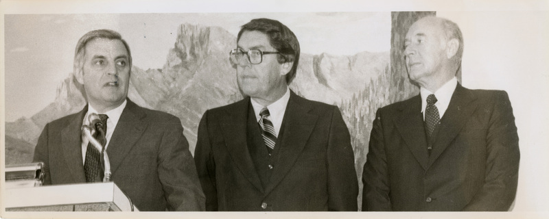 Photo Description: Governor Andrus, VP Mondale, and Lt. Governor Evans standing at a podium and speaking. Text back translation "Vice President Walter Mondale (D) John Evans: Lt. Governor Preside Governor Cecil Andrus" Notes read on back "5x3 3/5 100% Page C-6 The Veep Speaks"