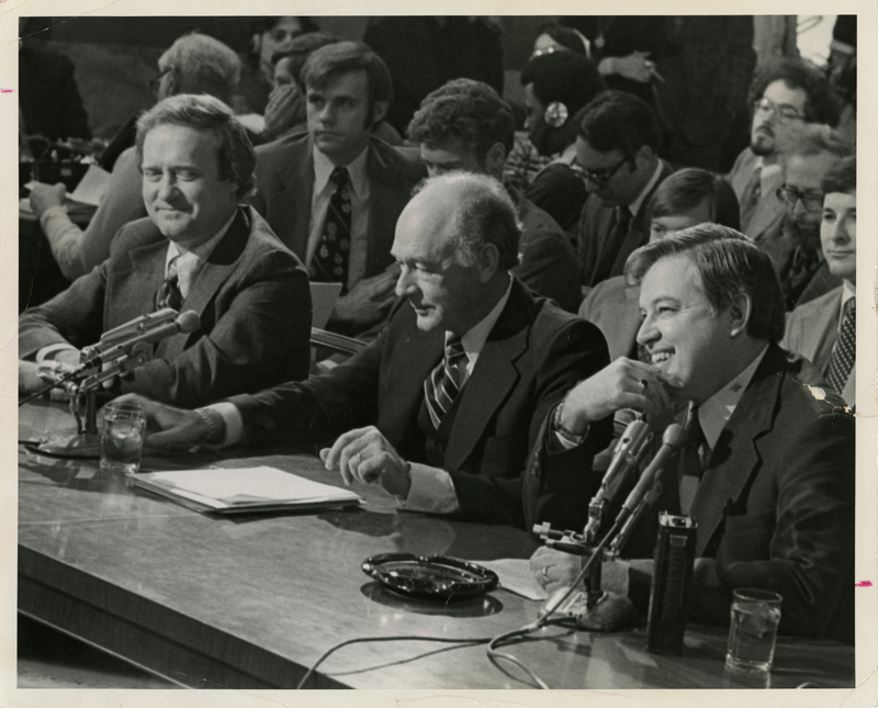 Photo Description: Senator James McClure, Governor Cecil Andrus, and Senator Frank Church sitting at a panel and smiling. Text back translation "Senator James McClure (R), Governor Cecil D Andrus (D), Senator Frank Church (D) the powerful Idaho political" Notes read on back "3x4 Washington, D.C. return to Ben Plastino"