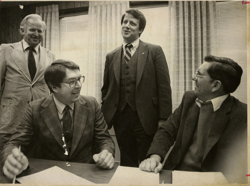 Photo Description: Senator Bob Saxuik, Governor John V Evans, Member of Northwest Power Planning Council Chris Carlson and BPA Administrator Peter Johnson are sitting at a desk and discussing energy needs. Notes read on back "FRI. P. A-2 about 1980. 4x5 3/8 86%"