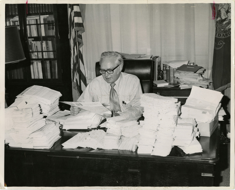 Photo Description: Idaho Representative Orval Hansen (R) is at this desk staring at a file while papers fill his desk.  Notes read on back "2 Col x 3 1/2 46"