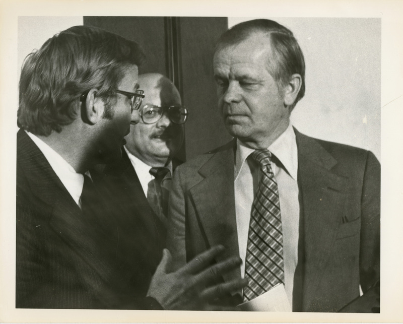 Photo Description: Senator Frank Church talks to two unknown people and is gesturing with his hands. Notes read on back "100% 3x4 1/2 Talking it over; 7am Thursday; Talking it over 24 [illegible]; 3 ed Boise - Two Jefferson County"