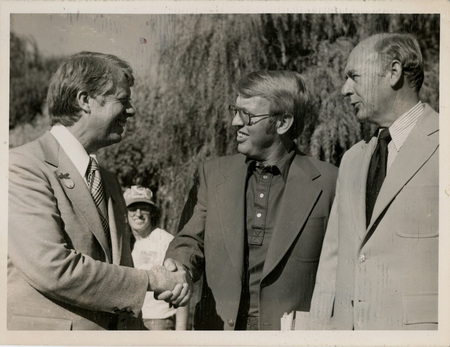 Photo Description: Governor Carter and Attorney General Park are smiling and shaking hands with Governor Andrus (D) right next to them also smiling. Text back translation "Governor Jimmy Carter (D) Attorney General Tony Park (D) Governor Cecil Andrus (D)"