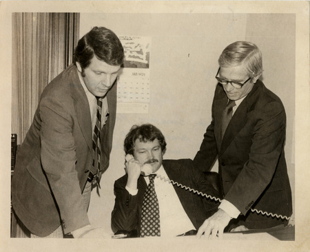 Photo Description: Idaho State Senators Kermit Kiebert (D), Senator Ron Twileger (D), and Senator Mike Mitchell (D) are all crowded around a desk reading some papers. One of them is on leaning back and on the phone. Notes read on back "Page C6 Top Democrat Senators 3x4 1/2 99"