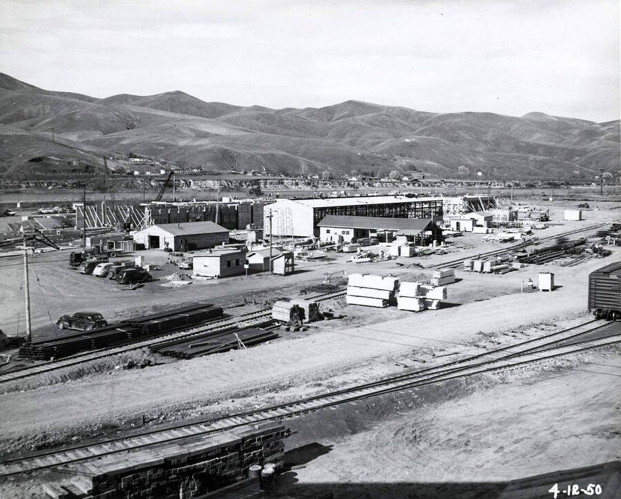 Several of the Clearwater mill's buildings under construction. In the foreground, stacks of lumber sit next to train tracks. The date written on the photograph is 4/12/1950.