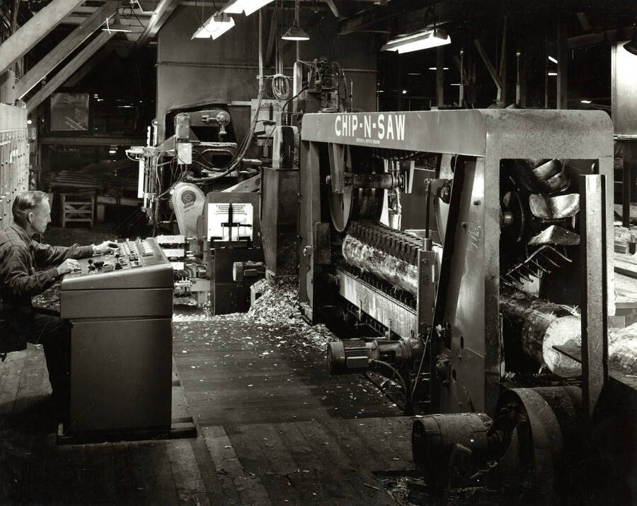 A man operates a piece of machinery at the Clearwater Paper Mill. The machine is labeled as a Chip-N-Saw. Description on the back reads 'Chip-N-Saw equipment shown above is part of a small log mill installation recently made at the Clearwater Unit sawmill of Potlatch Forests, Inc. in Lewiston. The installation is part of an extensive three year remolding project that is scheduled for completion next year.' The date listed on the photograph is August 1968.