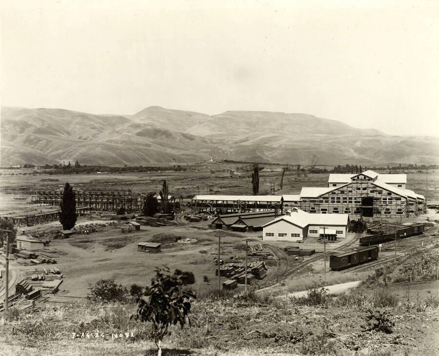 Construction of the buildings at the Clearwater plant. On the left side, the framing has just begun for one building while on the right hand side, the building is almost complete. Piles of lumber sit in the middle of the picture. Written on the picture is '7/26/1926 No. 82.'