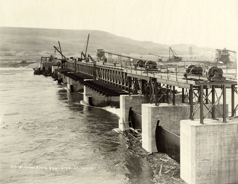 Water spills through the Lewiston dam. In the background, a small portion of the mill is visible. Written on the photograph is 'Dam, Lewiston. 4/28/1927 No. 256.'