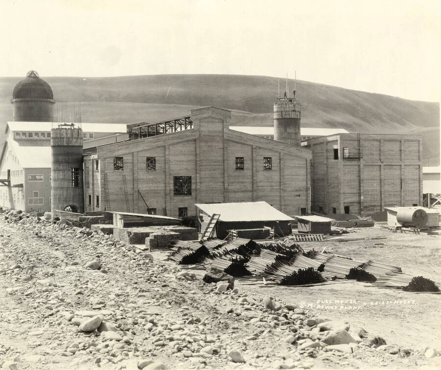 Two buildings at the Lewiston Mill are under construction. In front of the buildings are piles of construction materials. Written on the photograph is 'Lewiston fuel house and power plant. 4/20/1927 No. 153.'