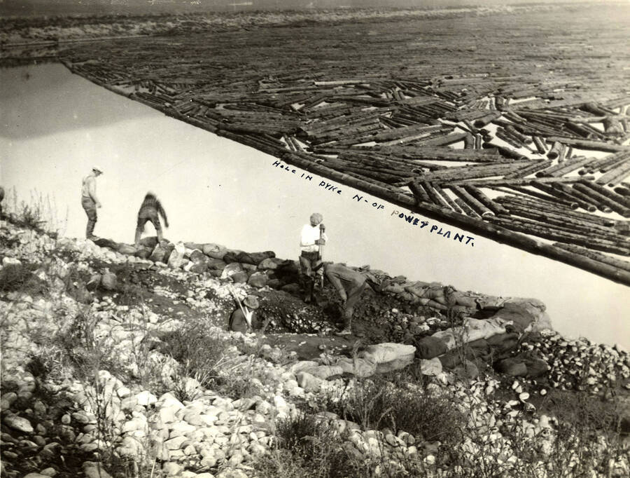 Men work on the dyke north of the power plant. Logs are visible in the center to back of the photograph. Written on the photograph is 'Hole in dyke N. of power plant.'