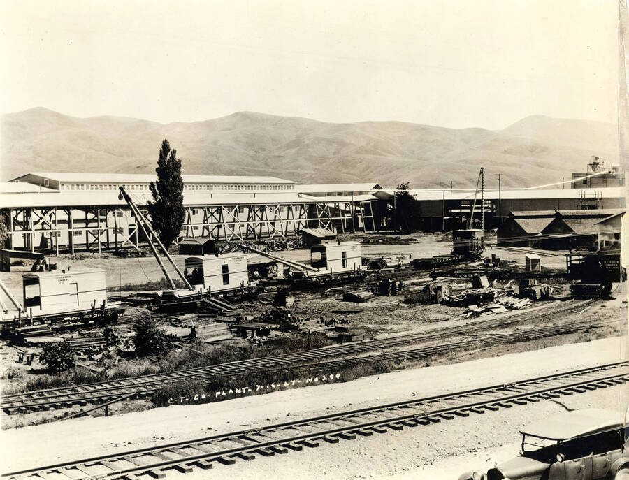 Three cranes sit on railroad tracks waiting to be used for construction. In the background is one of the mill buildings under construction. Written on the photograph 'CT CO Plant 7/16/1927 No. 289.'