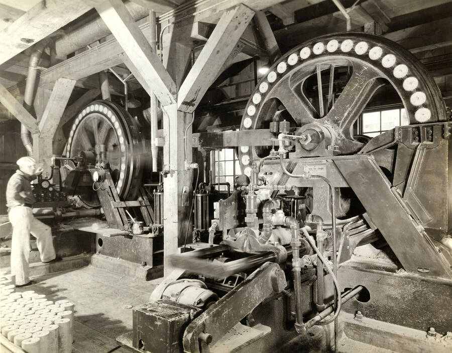 A worker operates a piece of machinery in one of the mills. The description on the back says 'Operating the Pres-To-Log machine. Potlatch Forests, Inc.' Also on the back of the photograph is the stamp for the photographer which reads 'Photographs from A. J Baker 3033 N. E. Sandy BLVD, Portland Oregon.'