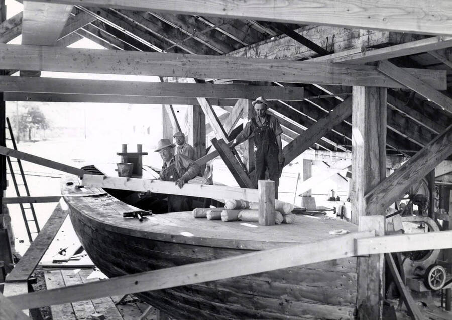 Three men work on building a boat for the log pond. Description taking from the back of the photograph.